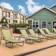 A wooden deck with lounge chairs and umbrellas in front of a building. at Central on the Green Apartment Homes, Raleigh