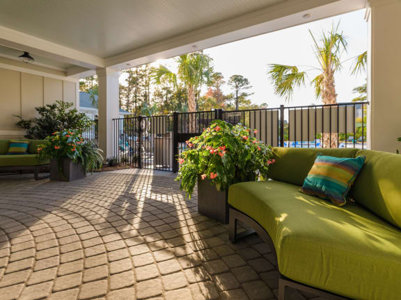 a covered patio with a green couch and potted plants