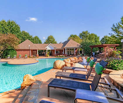 Resort-style swimming pool with lounge chairs, lush landscaping, and clubhouse at Village at Almand Creek apartments in Conyers, GA. Perfect for relaxation and outdoor living.