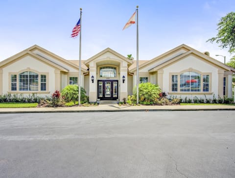 Leasing office exterior with two flag poles and neatly manicured landscaping along the entrance and sidewalk.