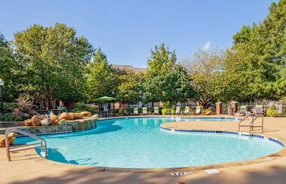 Resort-style swimming pool with waterfall feature, lush landscaping, and lounge seating at Village at Almand Creek apartments in Conyers, GA. Ideal for relaxation and outdoor enjoyment.