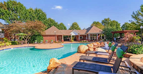 Resort-style swimming pool with lounge chairs, lush landscaping, and clubhouse at Village at Almand Creek apartments in Conyers, GA. Perfect for relaxation and outdoor living.