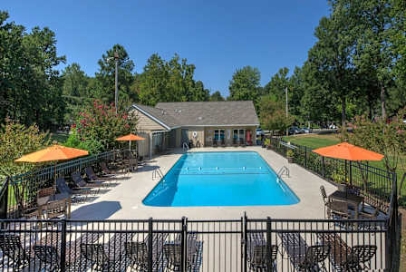 A pool surrounded by a black fence and orange umbrellas.