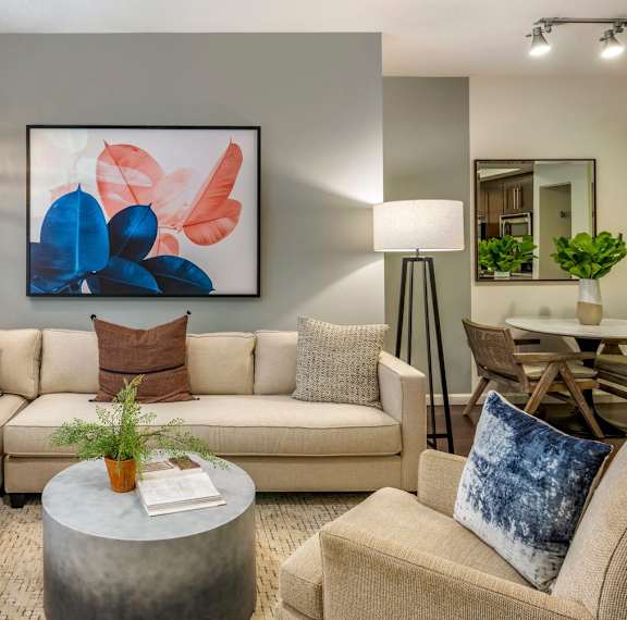 A living room with a beige couch, a grey coffee table, and a large abstract painting on the wall.