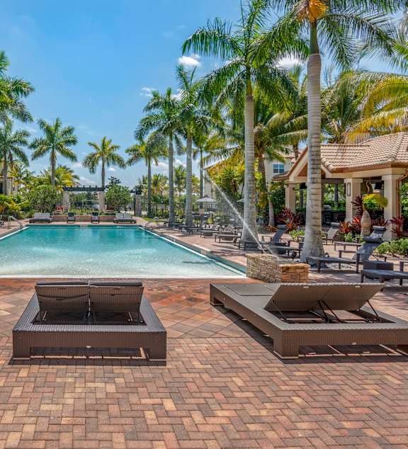 A pool surrounded by palm trees and lounge chairs.