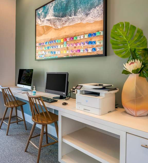 A room with a desk, chairs, and a large painting of a beach scene.