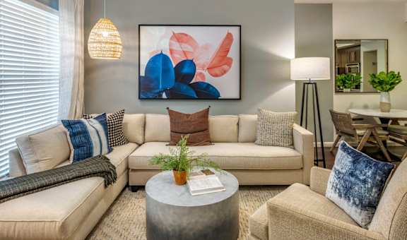 A living room with a beige couch, a grey coffee table, and a large abstract painting on the wall.