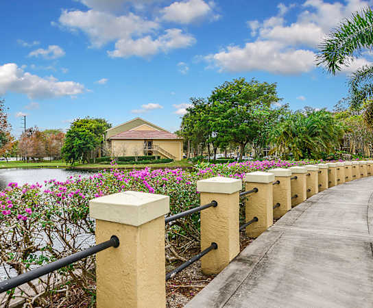 a bridge over a pond with flowers and a house in the background at Cypress Shores, Coconut Creek