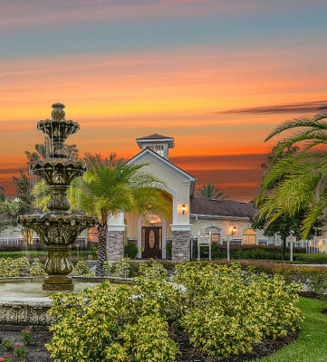 a fountain in front of a house with a sunset in the background