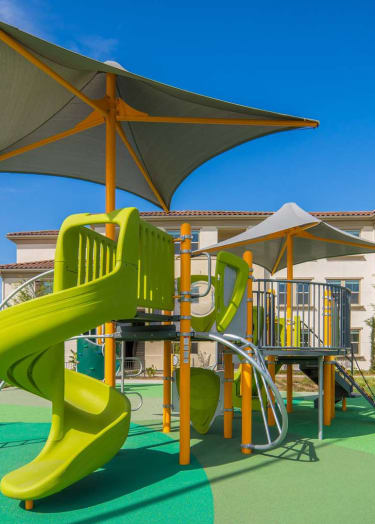 a playground with a slide and umbrella at villas at houston levee west apartments in
