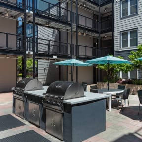 an outdoor patio with two bbq grills and umbrellas