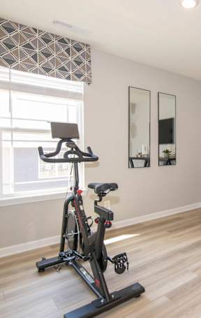 A room with a wooden floor and a black exercise bike.