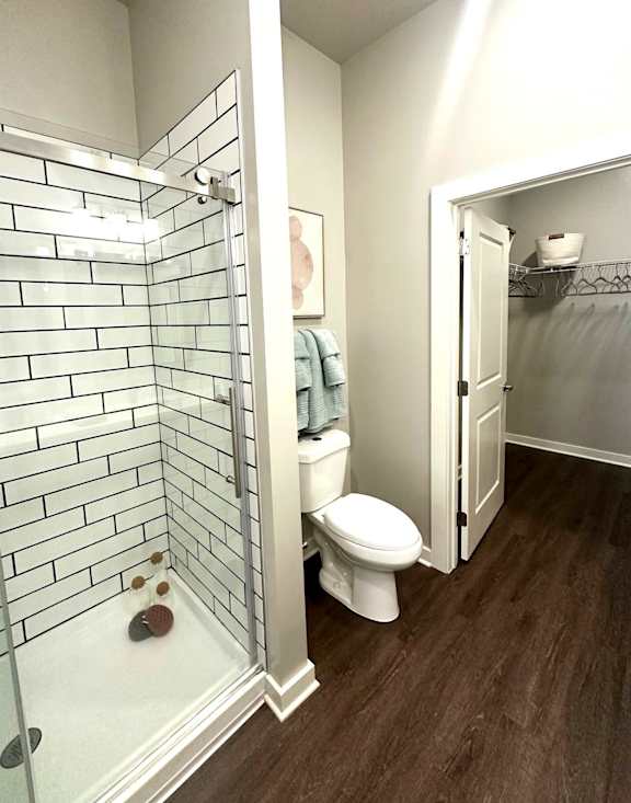 A white toilet in a bathroom with a glass shower door at The Percy Apartments, Nashville, TN, 37214