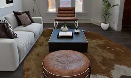 A living room with a white couch, a brown ottoman, and a brown rug.