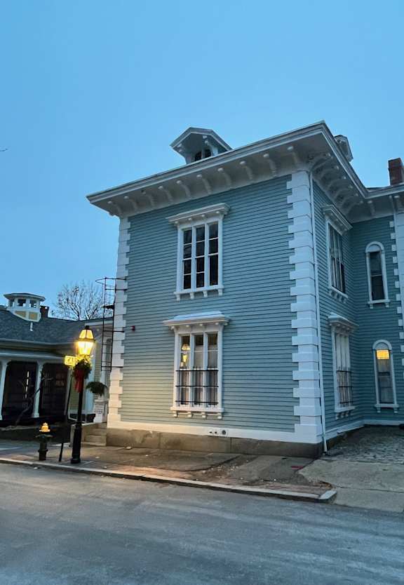 A blue house with white trim and a black iron railing on the porch.