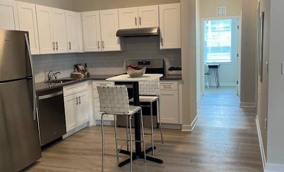 A kitchen with a refrigerator, sink, and a dining table with two chairs.
