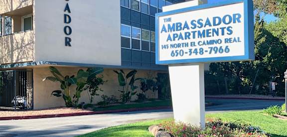 A building with a sign that says "The Ambassador Apartments" in front of it.