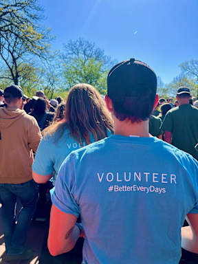A man wearing a blue shirt with the word "VOLUNTEER" on it is standing in a crowd.