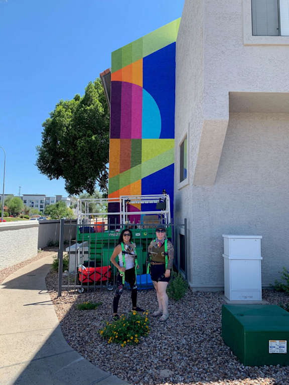 Two people standing in front of a colorful building.