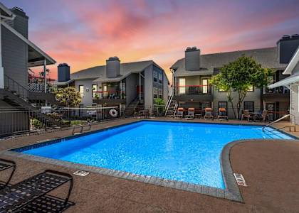 A swimming pool surrounded by patio furniture and houses.