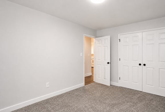 A room with white walls and a carpeted floor with two doors.