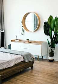 A bedroom with a bed, a mirror, and a plant.