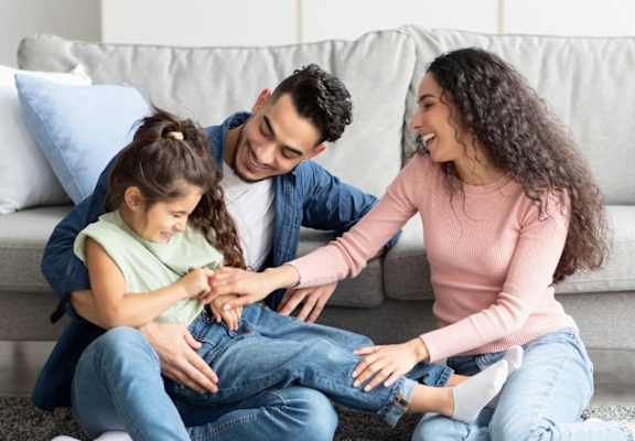 A family of three is sitting on the floor in a living room.