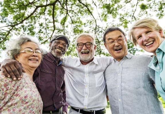 5 happy elderly people standing together, linking arms