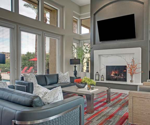 The resident lounge with TVs, fireplaces, windows and glass doors showing the outdoor pool area, couches, decorations, plush chairs, coffee tables, and French doors to the pool area at Mirador Apartments. 