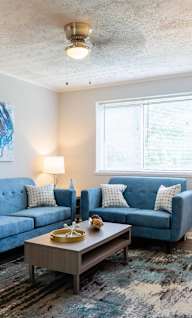 A living room with a blue couch and a painting on the wall.