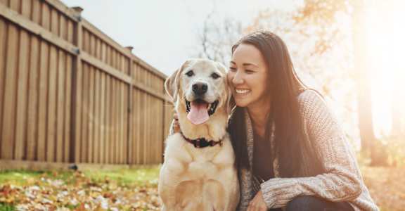 A woman is squatting down to the level of a happy dog in a backyard at The Vineyards Apartments, Tennessee
