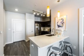 Kitchen island with white quartz countertops, modern lighting fixtures looking into kitchen