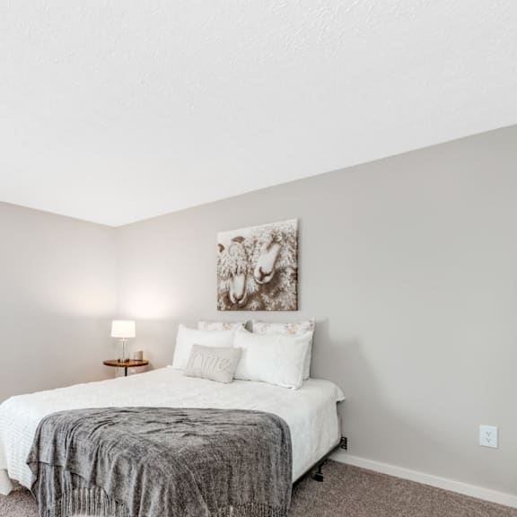 A bedroom with a bed, lamp, and painting on the wall.