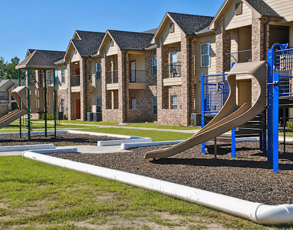 A playground with a slide and a building in the background.