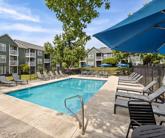 A swimming pool surrounded by lounge chairs and umbrellas in a sunny day.