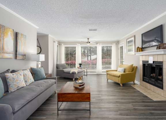 A living room with floor-to-ceiling windows, wood-look flooring, a ceiling fan, and a fireplace at Summerchase at Riverchase in Hoover, Alabama.