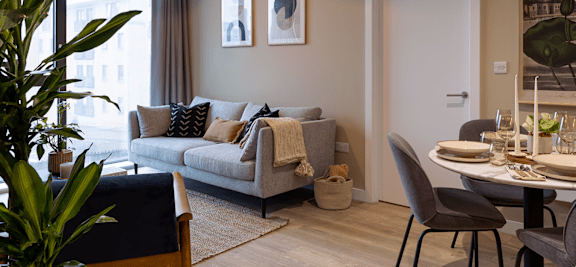 A living room with a grey couch and a dining table set for two.