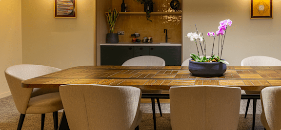 A dining table surrounded by chairs and a flower pot on the table.