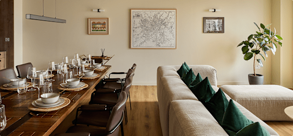 A dining table set for a meal with a couch and a potted plant in the background.