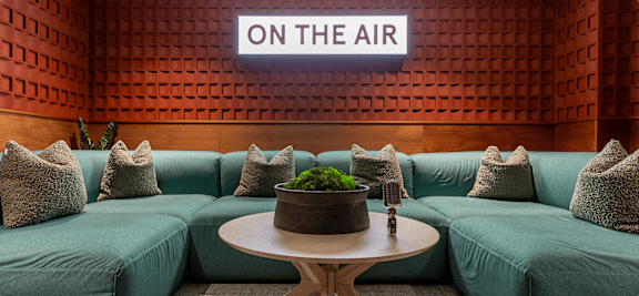 A modern living room with a large couch and a sign that says "ON THE AIR" on the wall.