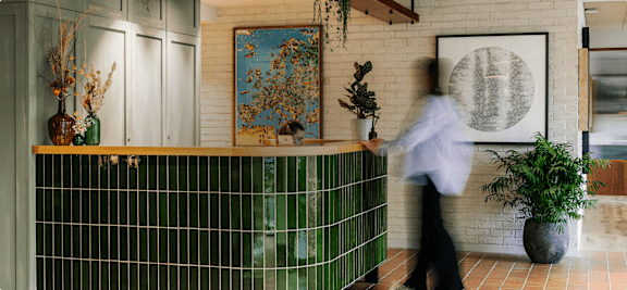 A person in a white shirt and black pants walks past a green tiled counter.