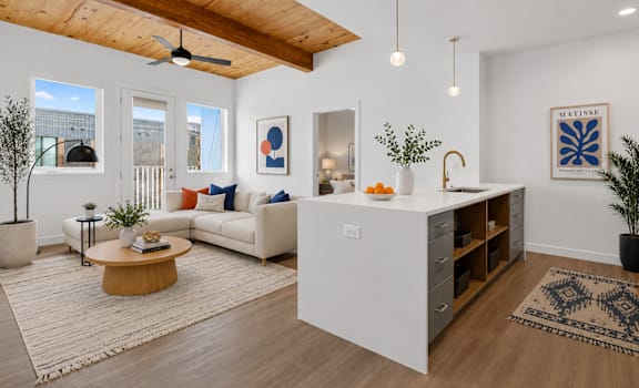 A modern kitchen with a white island and a white couch with orange pillows.