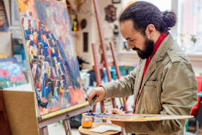 A man with a beard is painting a picture on a canvas.