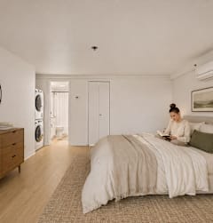 A woman is sitting on a bed in a room with wooden floors and furniture.