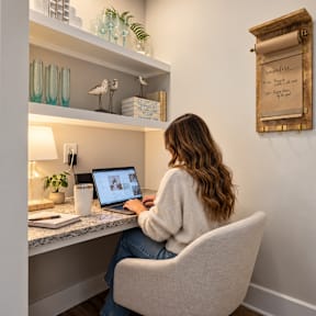 A woman is sitting at a desk with a laptop and a cup in front of her.