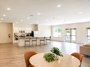 A dining room with a table and chairs in the foreground and a kitchen in the background.