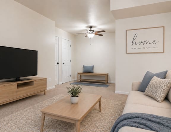 A living room with a flat screen TV, a coffee table, a couch, and a ceiling fan.
