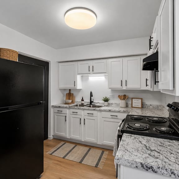 A black refrigerator stands in a kitchen with white cabinets and a marble countertop.