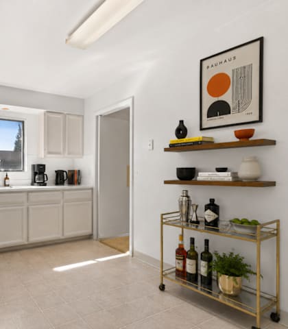 A kitchen with white appliances and a trolley with bottles on it.