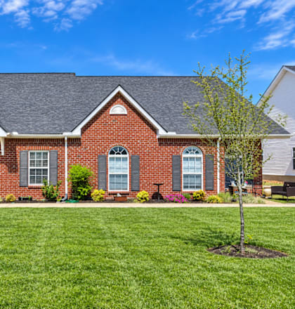 A red brick house with a grey roof and a green lawn in front.